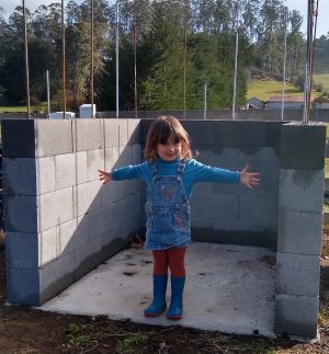 Child standing on a small cement pad, surrounded on three sides with a low brick wall.